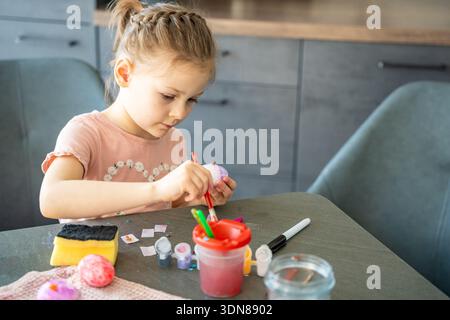 Child painting Easter eggs with brushes and colorful paints at table at home, top view. Creative Easter craft process, festive preparation and hands Stock Photo