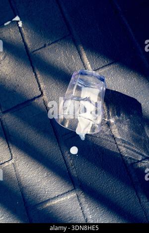 Spilled milk from a plastic cup on a textured dark pavement under sunlight and shadow. Miami, Florida, USA Stock Photo