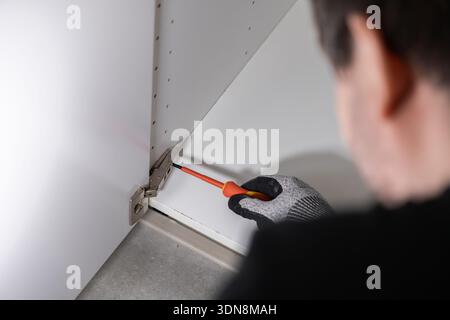 Close-up view of a craftsman's hand in protective glove tightening a silver hinge on a white cabinet, emphasizing quality construction and detailed in Stock Photo