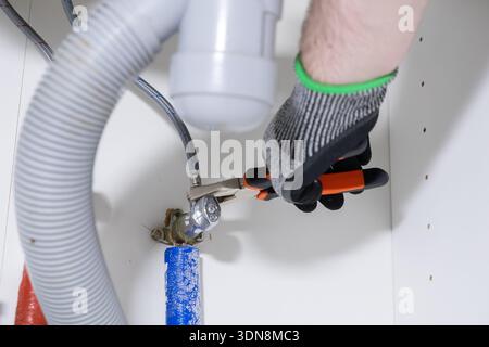 Detailed view of a worker's gloved hand adjusting a vital plumbing pipe connection with a wrench under a sink, emphasizing expert home repair and DIY Stock Photo
