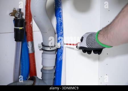 A person's gloved hand precisely tightening a screw on diverse plumbing pipes and drainage components, illustrating a crucial home renovation or repai Stock Photo
