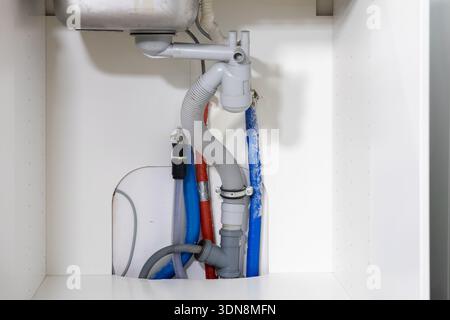 View inside a white cabinet showing the intricate kitchen sink plumbing setup, including drainage, water lines, and various connections, vital home in Stock Photo