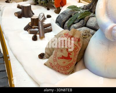 Commercial holiday display features burlap Reindeer Mail 25th December sacks, wooden logs, pine cones on faux snow, for festive seasonal retail decor Stock Photo