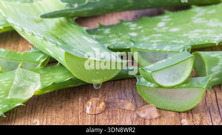 Dripping juice from sliced pure aloe vera leaf on wooden board. Sliced aloe vera leaves with transparent gel drops closeup. Component of healthy food Stock Photo