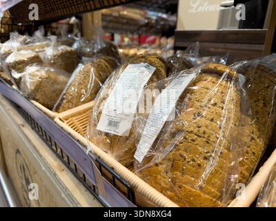 Poznan, Poland - November 28, 2025: Fresh whole grain bread loaves, pre-sliced and plastic-wrapped, neatly arranged in wicker baskets on retail shelve Stock Photo