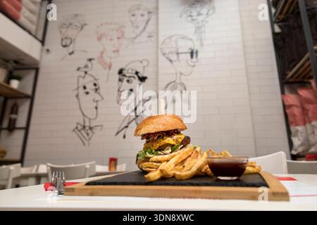 mouth-watering gourmet cheeseburger in a toasted brioche bun, served on a rustic wooden board with a side of crispy golden fries and savory dipping sa Stock Photo