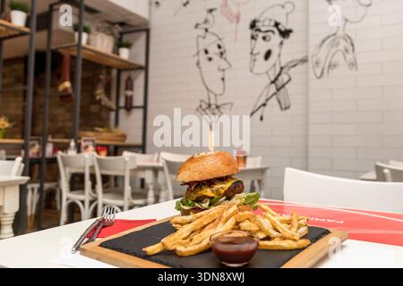 mouth-watering gourmet cheeseburger in a toasted brioche bun, served on a rustic wooden board with a side of crispy golden fries and savory dipping sa Stock Photo