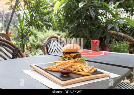 mouth-watering gourmet cheeseburger in a toasted brioche bun, served on a rustic wooden board with a side of crispy golden fries and savory dipping sa Stock Photo