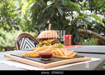 mouth-watering gourmet cheeseburger in a toasted brioche bun, served on a rustic wooden board with a side of crispy golden fries and savory dipping sa Stock Photo
