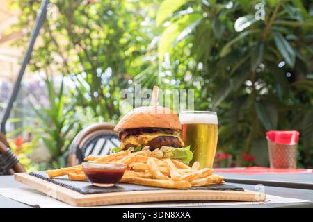 mouth-watering gourmet cheeseburger in a toasted brioche bun, served on a rustic wooden board with a side of crispy golden fries and savory dipping sa Stock Photo