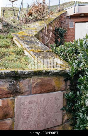 Old German water tank memorial plaque dated 1950 and 1969 on weathered red sandstone wall with green moss covered concrete roof and vegetation in back Stock Photo