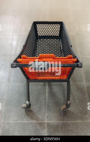Shopping cart features a striking orange basket with a black mesh design, placed on a smooth tiled floor, highlighting its practical use in retail env Stock Photo