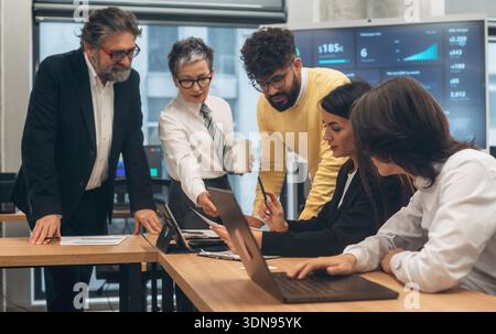 Diverse team of business professionals engaged in collaboration within a modern office environment, analyzing data on laptops and discussing strategie Stock Photo