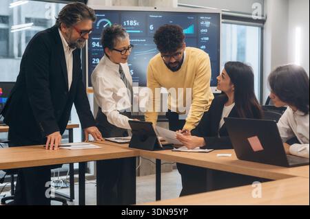 Diverse team of business professionals engaged in collaboration within a contemporary office, analyzing data on digital screens while discussing strat Stock Photo