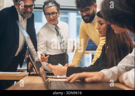 Diverse team members engaged in a collaborative discussion around a laptop in a contemporary office, sharing insights and strategies for effective pro Stock Photo