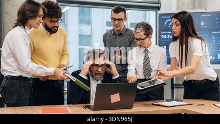 Diverse team of business professionals engaged in a collaborative meeting in a modern office, analyzing data on laptops and tablets, highlighting team Stock Photo