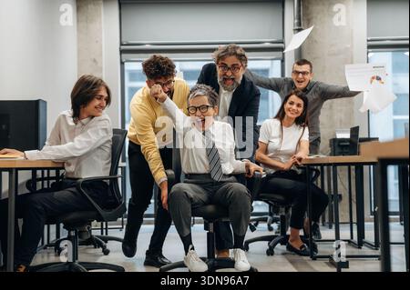 Diverse team of office workers is celebrating success in a modern business office, with expressions of joy and collaboration, highlighting teamwork an Stock Photo