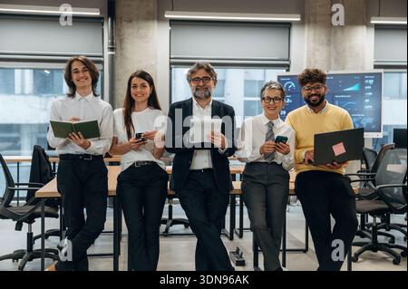 Diverse group of business professionals stands confidently in a modern office, showcasing teamwork and collaboration, with sleek furniture and technol Stock Photo