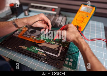 Technician's hands are meticulously repairing an electronic device, using a digital multimeter to measure components on a circuit board Stock Photo