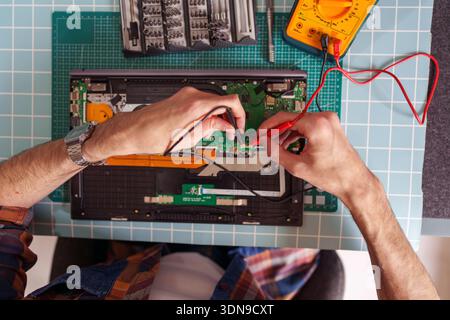 Hands of a technician using a multimeter to check the circuit board of an open laptop, performing electronic repair and diagnostics Stock Photo