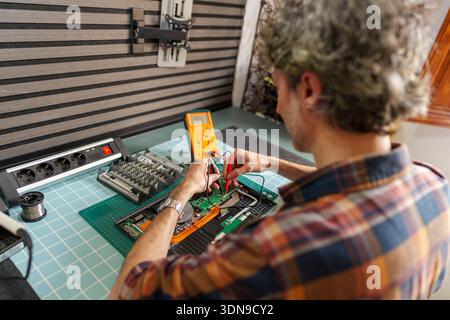 Technician checking electronic device circuit board with multimeter, diagnosing and repairing hardware problem Stock Photo
