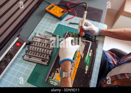 Technician repairing internal components of a computer, using a soldering iron and various repair tools Stock Photo