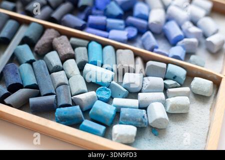 Set of soft pastel crayons in blue, teal in a wooden artist's box. Broken crayons, top view. Art supplies. Stock Photo
