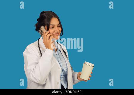 Young female physician communicating on cell phone and drinking coffee Stock Photo