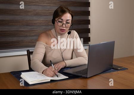 Female writer taking notes while working on laptop Stock Photo