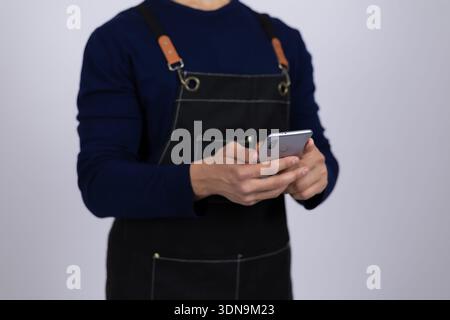 Service worker in apron using smartphone in studio Stock Photo