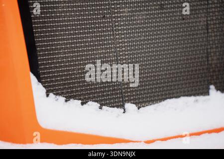 Detailed shot of black mesh ventilation screen framed by orange machinery casing, with snow drift resting on the base for winter equipment storage con Stock Photo