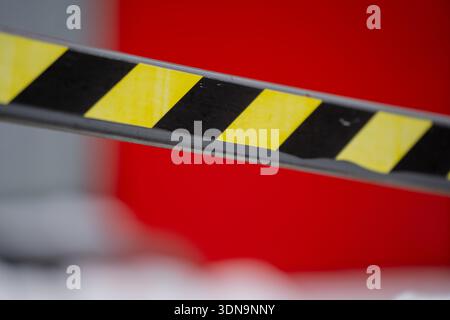 Selective focus detail of striped safety barrier beam in black and yellow, emphasizing hazard warning pattern against out of focus red construction eq Stock Photo