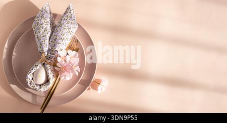 Easter Table Setting with Bunny Napkin and Decorated Egg.  Festive Spring Arrangement on Pink Background Stock Photo