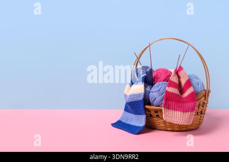 Blue, pink and beige knitting balls in basket with knitting needles and knitted scarf on pink background. Set for the hobby of knitting warm clothes or toys. Concept needlework Stock Photo