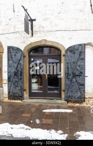 PTUJ, SLOVENIA, 01.04.2026:A historic doorway featuring heavy iron shutters, a stone arch, and a glass door, set on a whitewashed wall. Snow on the gr Stock Photo