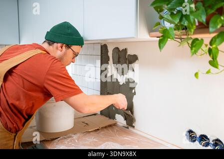 Master tiler installing ceramic kitchen backsplash, spreading adhesive with a trowel on the wall during a home renovation, diy or professional remodeling project Stock Photo