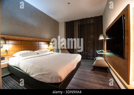 Modern hotel room in Warsaw, Poland featuring a king-size bed, warm lighting, contemporary decor, and a sleek, cozy atmosphere—ideal for hospitality Stock Photo
