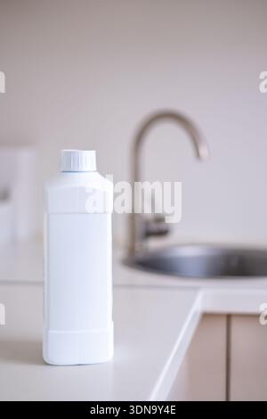 Blank white cleaning product bottle mockup positioned on a kitchen countertop, with a stainless steel sink and faucet visible in Stock Photo