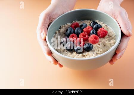 Close up of hands holding a ceramic bowl filled with nutritious porridge topped with fresh forest fruits on a warm background Stock Photo