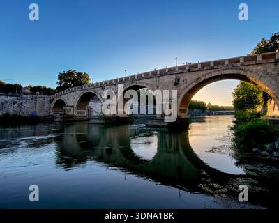 Historic stone bridge crossing the river Tiber with St Peter's Basilica in background in Rome, Italy at dawn Stock Photo