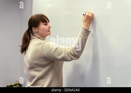 Woman engaged in writing on a whiteboard in a contemporary office, illustrating teamwork and brainstorming in a creative atmosphere filled with inspir Stock Photo