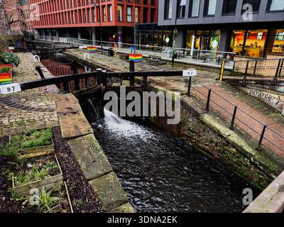 Manchester, UK - January 22, 2026: Canal lock in Manchester features flowing water, brick walls, and colorful LGBT rainbow planters along the canal. Stock Photo