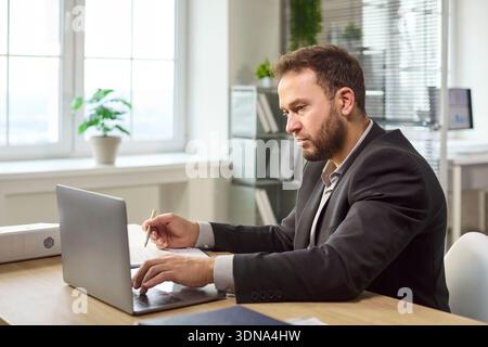 Serious businessman working on laptop in modern office, planning and data analysis Stock Photo