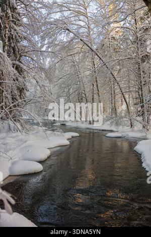 Espoo, Finland - December 31, 2023: Picturesque view of a flowing river in a snow-covered forest during winter sunset. Stock Photo