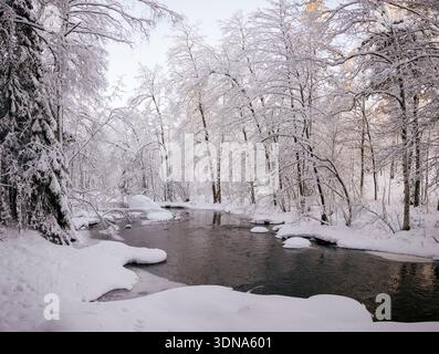 Espoo, Finland - December 31, 2023: Picturesque view of a flowing river in a snow-covered forest during winter sunset. Stock Photo