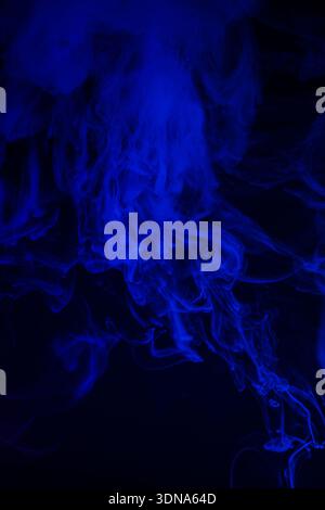 Thick curling blue smoke in dark environment Stock Photo
