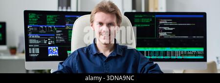 Portrait of Young Man Smiling While Working with Computer Screens Stock Photo