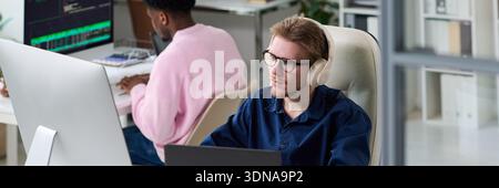 Young Man Wearing Headphones Working at Computer in Office Stock Photo