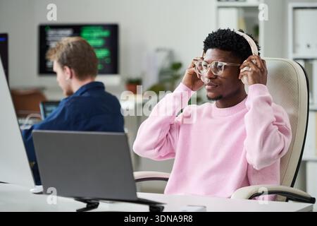 Young Black Man Wearing Headphones Working at Computer in Office Stock Photo