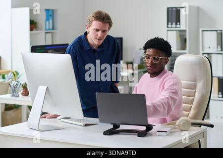 Young Man and Young Black Man Collaborating at Office Desk Stock Photo